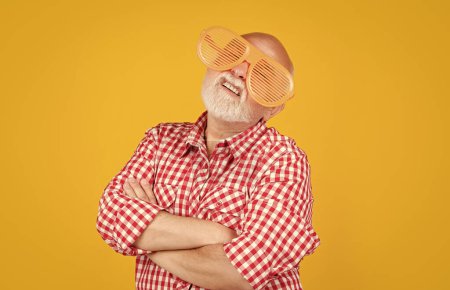 senior man with party glasses on yellow background.