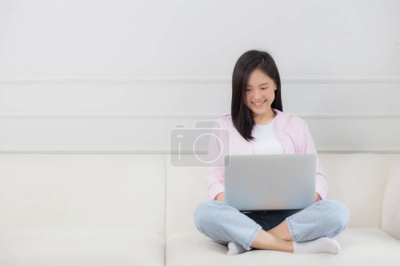 Young asian business woman work from home with laptop computer online to internet on sofa in living room, freelance girl using notebook sitting on couch with comfort and relax, lifestyles concept. Poster 658267054