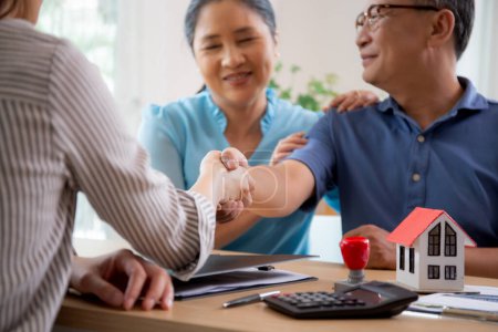 Happy couple elderly handshake with mortgage officer with agreement approve of buying home with loan, senior talking with agent real estate for planning while shaking hands, business and rent concept.