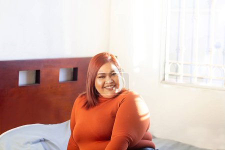 Foto de Joven modelo de talla grande sonriendo sentada en su cama. mujer mexicana con sobrepeso - Imagen libre de derechos