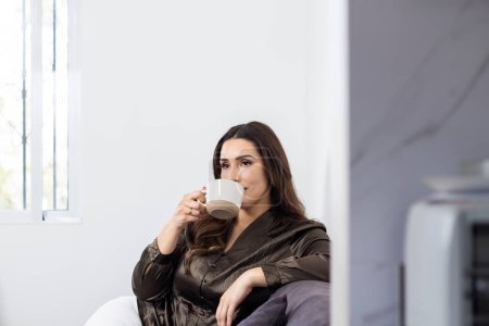 schöne junge hispanische Frau sitzt zu Hause und trinkt eine Tasse Kaffee