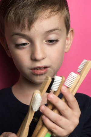 Foto de A small boy of Slavic appearance holds many bamboo toothbrushes in his hands on a pink background - Imagen libre de derechos