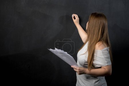 Foto de Una mujer de apariencia europea escribe con tiza en un muro de pizarra. Profesor en clase - Imagen libre de derechos