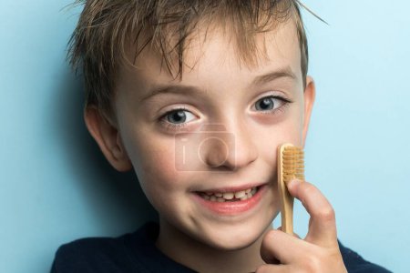 Foto de Un niño pequeño sostiene un cepillo de dientes de bambú cerca de su cara. eco amigable - Imagen libre de derechos