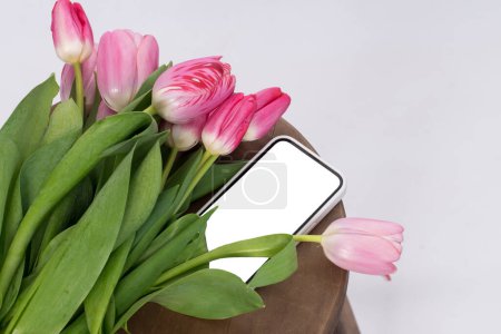Foto de Maqueta de un teléfono inteligente cerca de un ramo de tulipanes rosados. lugar para el texto. - Imagen libre de derechos