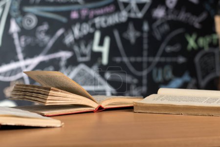 Photo for Open books lie on a desk or table against a chalk-painted chalkboard wall - Royalty Free Image