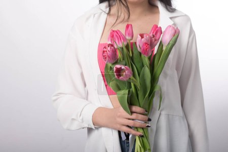 Foto de Un ramo de tulipanes rosados en las manos de una niña sobre un fondo blanco. una foto sin rostro - Imagen libre de derechos