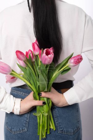 Foto de La chica sostiene un ramo de tulipanes rosados detrás de ella. - Imagen libre de derechos