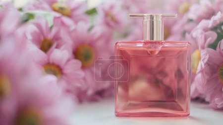 Foto de Una botella de perfume rodeada de flores de crisantemo rosa. Eau de toilette, eau de parfum, concepto de belleza. - Imagen libre de derechos