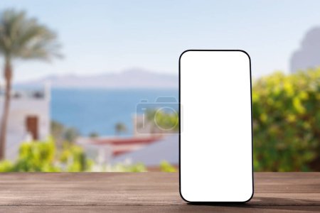 Photo for Smartphone mockup on wooden table against blurred seaside background - Royalty Free Image