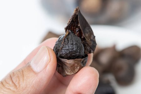 Photo for Closed up picture of someone hand holding peel black garlic with blur background of black garlic heaps. - Royalty Free Image