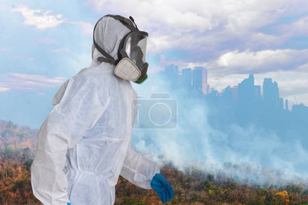 Un agent portant une combinaison de protection blanche et un masque à gaz intégral à l'ombre des grandes villes est menacé par la pollution atmosphérique causée par la fumée des feux de forêt et les effets du réchauffement climatique sur le fond.