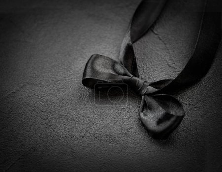 Téléchargez les photos : Un noeud de ruban de satin noir repose sur un fond noir. Concept Black Friday - en image libre de droit