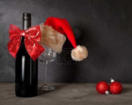 Téléchargez les photos : Une bouteille de vin, un verre avec un chapeau de Père Noël sur un fond de branches de sapin. Composition de Noël. - en image libre de droit