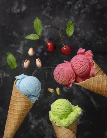 Téléchargez les photos : Trois cônes de gaufres avec crème glacée, rose, bleu, vert, baies, fraises, pistaches sur fond sombre - en image libre de droit