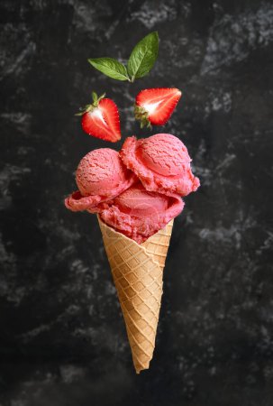 Téléchargez les photos : Glace aux fraises avec des fraises dans un cône de gaufre sur un fond sombre - en image libre de droit