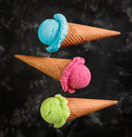 Téléchargez les photos : Trois cônes de gaufres avec crème glacée, rose, bleu, vert, baies, fraises, pistaches sur fond sombre - en image libre de droit