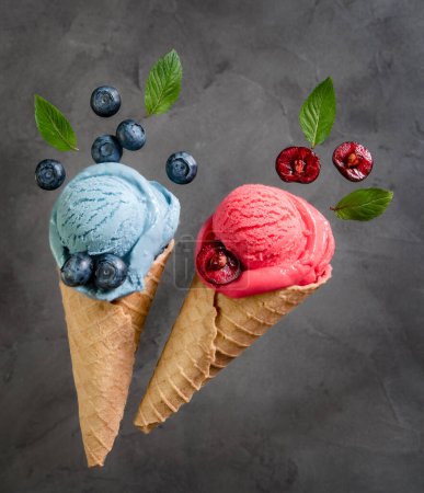 Téléchargez les photos : Glace bleue et rose aux baies dans un cône de gaufre aux myrtilles et cerises sur fond gris - en image libre de droit