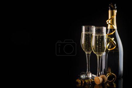 Foto de Dos copas de champán, velas y una botella sobre fondo negro. Concepto de celebración de Año Nuevo y Navidad. - Imagen libre de derechos