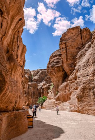Foto de Petra, Jordania - 16 de abril de 2023: La gente camina en el Siq, la entrada principal a la antigua ciudad de Nabatea. Es un desfiladero oscuro y estrecho que termina en el Tesoro.. - Imagen libre de derechos
