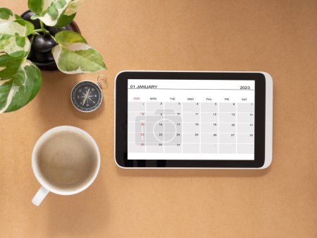 Draufsicht, Tablet mit Kalenderblatt Januar 2023 und Baum, Kaffeetasse und Kompass. Geschäftskonzept und Ausbildung. Kalender-App mit Planung.