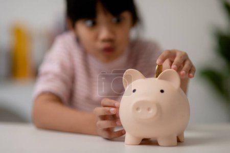 Foto de Niña asiática ahorrando dinero en una alcancía, aprendiendo sobre el ahorro, Kid ahorrar dinero para la educación futura. Concepto de dinero, finanzas, seguros y personas - Imagen libre de derechos