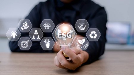Téléchargez les photos : Homme d'affaires main tenant ampoule avec icône esg sur écran virtuel, ESG Concept environnemental, social et de gouvernance d'entreprise - en image libre de droit