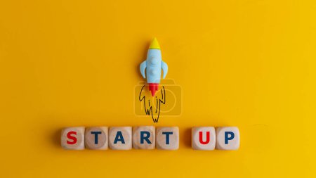 Startup-Konzept. Ein Symbol für den schnellen Start eines neuen Projekts in der Wirtschaft. Rakete und Würfel mit Text Start up auf gelbem Hintergrund.