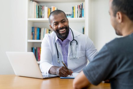 Laughing mature adult african american male doctor listening to patient at office of hospital