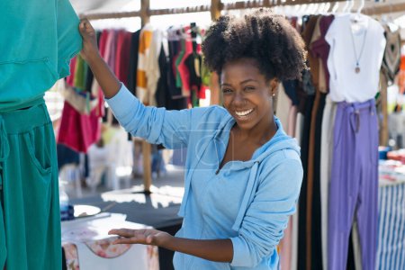 Foto de Beautiful african american woman selling clothes at flea market outdoor in city in summer - Imagen libre de derechos