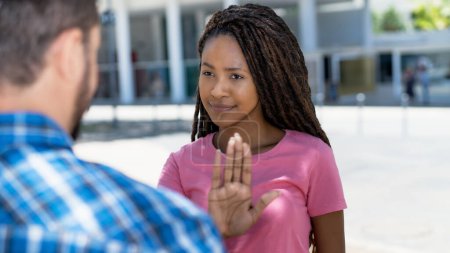 Téléchargez les photos : Femme noire confiante avec dreadlocks geste arrêt à l'homme blanc en discussion en plein air en ville en été - en image libre de droit