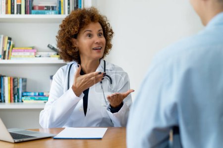 Téléchargez les photos : Rire mature médecin femme avec de bonnes nouvelles pour le patient au bureau de l'hôpital - en image libre de droit
