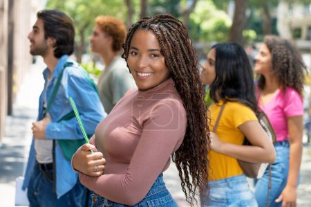 Foto de Hermosa estudiante universitaria afroamericana con grupo de adultos jóvenes caucásicos e hispanos al aire libre en la ciudad en verano - Imagen libre de derechos