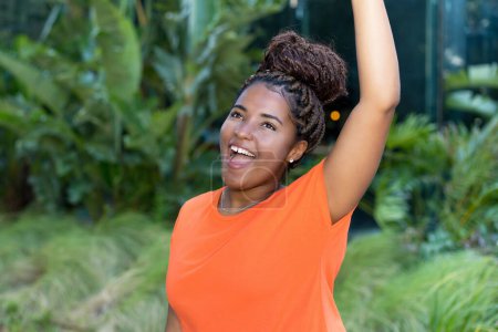 Téléchargez les photos : Succès encourageant jeune femme adulte africaine avec chemise orange dans une zone tropicale - en image libre de droit