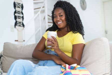 Téléchargez les photos : Belle corpulente afro-américaine jeune adulte buvant du café à l'intérieur à la maison - en image libre de droit