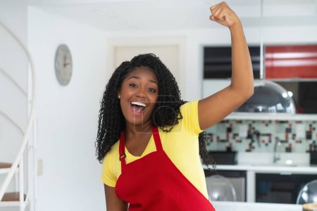 Foto de Retrato de au pair afroamericano motivado con delantal en el interior de la cocina moderna - Imagen libre de derechos