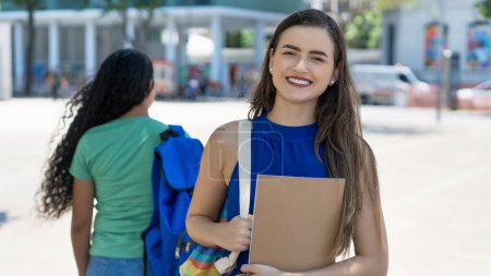 Caucasian female student with brunette hair and colorful backpack outdoor in city in summer