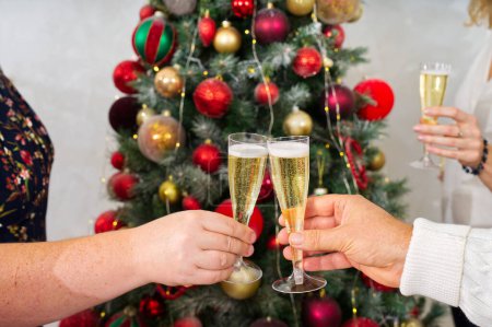 Foto de Año Nuevo o celebración de Navidad. Manos sosteniendo las copas de champán. Árbol de Navidad con guirnaldas en el fondo. - Imagen libre de derechos