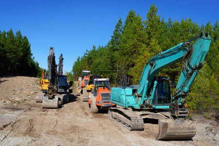 Photo for Heavy Construction Equipment, Tractors, Excavators, and Bulldozers Parked in a Forest Parking Lot. New Communication Line Installation - Royalty Free Image