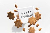 Canvas with text Happy Holidays flying, levitating with star cookies almonds. Group of tasty snacks around square canvas Isolated on white. Creative food arrangement, greeting card design. Poster #618349942