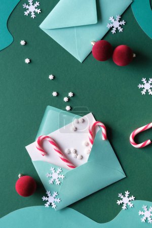 Photo for Writing Christmas greetings - quill and greeting cards in paper envelopes. Xmas background with candy canes, vibrant magenta trinkets, snowflakes. Top view, flat lay on green paper, text Merry Xmas on card. - Royalty Free Image