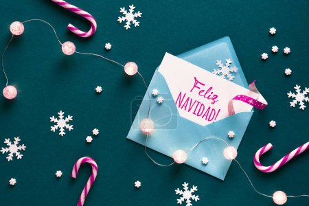 Photo for Feliz Navidad means Merry Christmas in Spanish language. Greeting card in paper envelope. Christmas background on green paper with magenta candy canes, lights garland, snowflakes . Top view, flat lay - Royalty Free Image