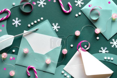 Téléchargez les photos : Carte de vœux dans une enveloppe papier. Fond de Noël sur papier vert avec cannes à bonbons rayées blanches et magenta, bibelots, guirlande de lumières, flocons de neige. Vue du dessus, mise à plat, espace de copie. - en image libre de droit