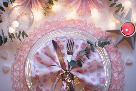 Téléchargez les photos : Noël, installation de table de Noël avec ventilateurs en papier rose, brindilles d'eucalyptus parfumées, bougies et guirlande légère et festive. Couché sur une table blanche cassée. Vue de dessus monochromatique. - en image libre de droit