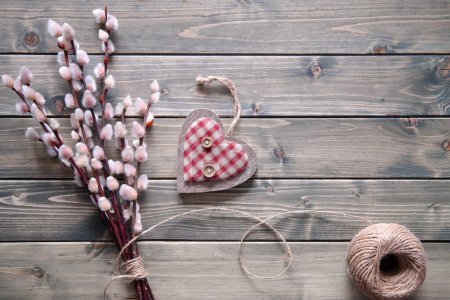 Foto de Rustic springtime background. Bunch of pussy willow twigs tied with hemp cord. Textile soft checkered heart with buttons. Flat lay, top view on rustic table, aged beige faded wooden planks. - Imagen libre de derechos