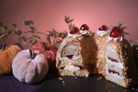 Foto de Pastel alemán Frankfurter Kranz o Frankfurt Crown Cake. Bisquit con crema de mantequilla y cerezas. Corta la mitad del pastel. Decoración otoñal con calabazas textiles y hojas secas. - Imagen libre de derechos