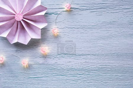 Photo for Paper fan, folded flower and string of festive lights, electric garland with pink glass balls. Copy-space on cracked wooden board. Festive Winter or Spring banner. Pace for text, flat lay, top view. - Royalty Free Image