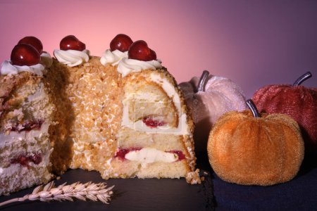Foto de Pastel alemán Frankfurter Kranz o Frankfurt Crown Cake. Bisquit con crema de mantequilla y cerezas. Corta la mitad del pastel. Decoración otoñal con calabazas textiles y hojas secas. - Imagen libre de derechos