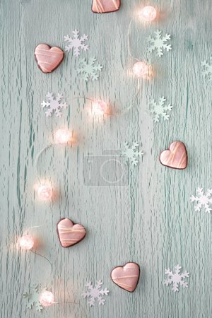 Photo for Winter pastel mint green background with paper snowflakes and string of shiny balls, electric Xmas garland and heart shape cookies. Simple minimal Winter holidays, Christmas background. - Royalty Free Image