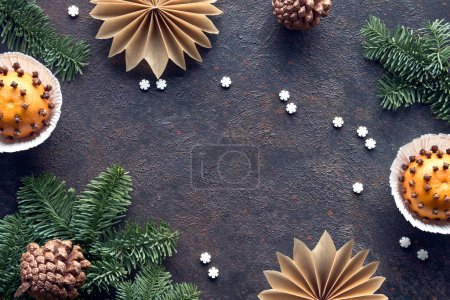 Photo for Wintertime dark background with fragrant pomander balls. Classical decorations - tangerine with cloves. Handmade paper stars from brown baking paper, pine cones, fir twigs and burning beewax candle. - Royalty Free Image